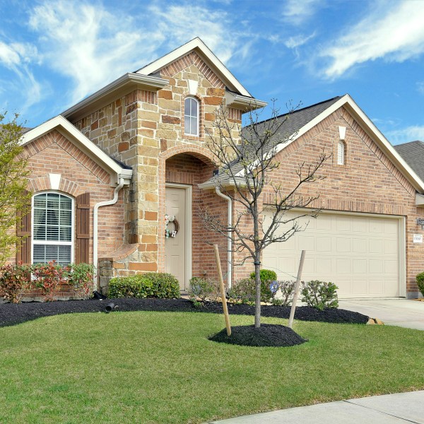 brick house with beautifully manicured lawn with green grass